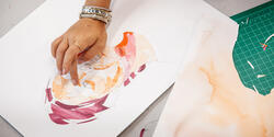 hand placing cut paper on a collage portrait