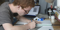 student with a laptop drawing at a desk