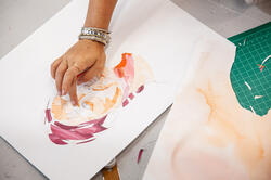 hand placing cut paper on a collage portrait