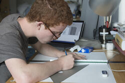 student with a laptop drawing at a desk