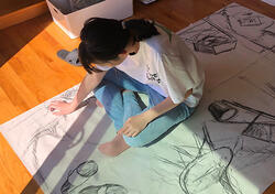 student drawing on large paper on the floor